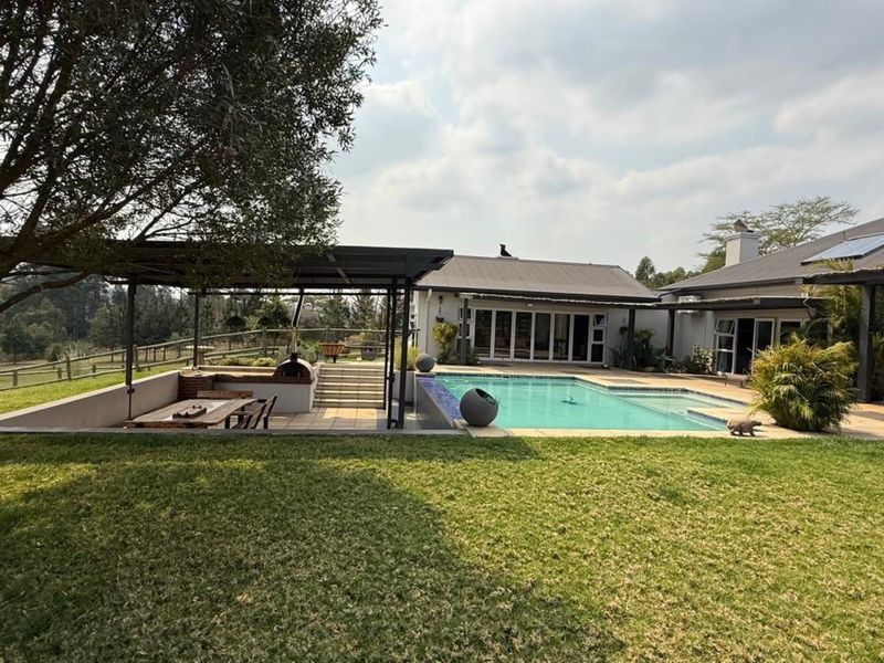 Spacious outdoor entertainment area featuring a swimming pool, covered patio with built-in braai, and well-maintained garden surroundings.