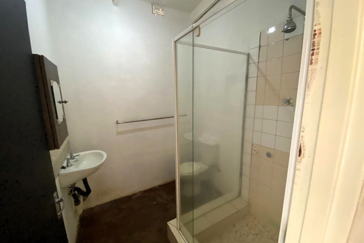 A functional bathroom featuring a shower enclosure, wall-mounted basin, and toilet, requiring cosmetic updates and repairs to finishes.