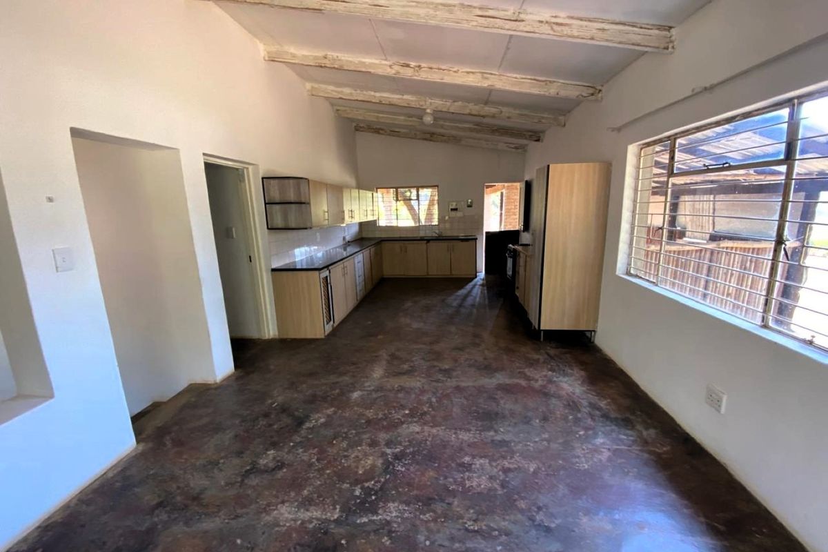 Spacious kitchen area featuring built-in cabinetry, polished concrete floors, and exposed timber ceiling beams, offering a blank canvas for renovation.