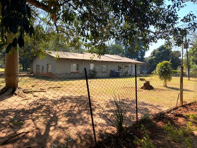 Rear view of a single-story dwelling on a small holding, featuring a corrugated metal roof and wire mesh perimeter fencing.