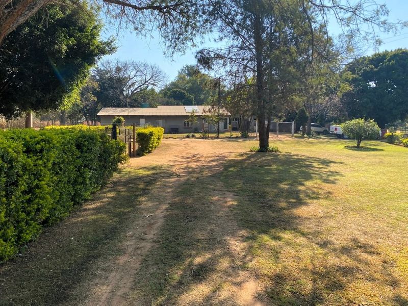 A view of the front exterior of the small holding, featuring a large garden, established trees, and a dwelling equipped with solar panels.