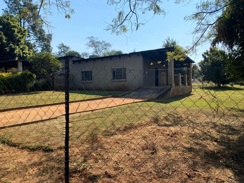 Front view of a small holding property featuring a simple structure with a concrete ramp entrance and corrugated iron roofing, set on a large plot.