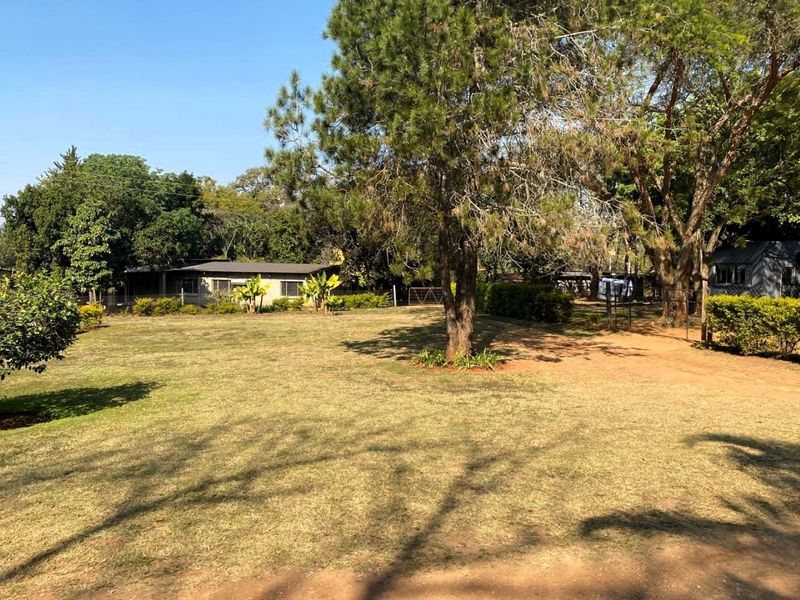 A spacious, well-established garden area featuring mature trees, expansive lawn, and perimeter fencing on a small holding property.