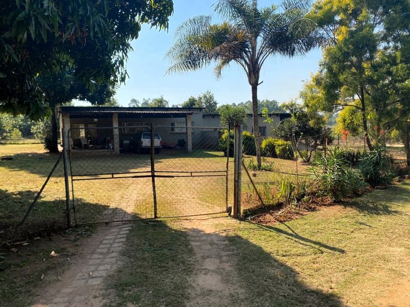 Front view of the small holding property featuring a gated entrance, paved driveway, and a covered patio area set within a landscaped garden.