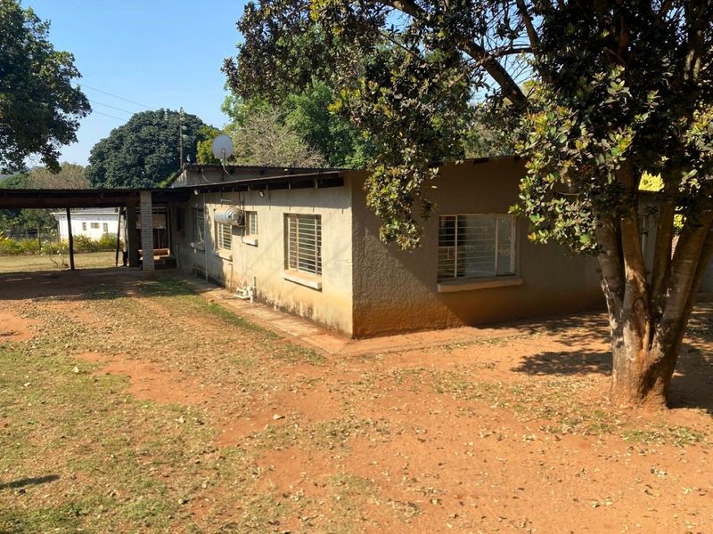 Rear view of the property showing the exterior wall, metal window frames, a covered patio area, and an external geyser installation.