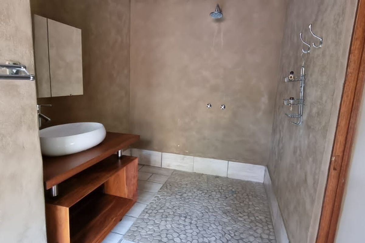 A modern bathroom featuring a vessel sink on a wooden vanity, a pebble-tiled shower floor, and a wall-mounted shower head with textured wall finishes.