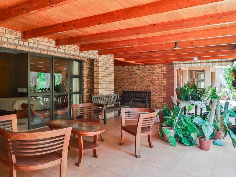 A spacious covered patio featuring exposed timber beams, facebrick walls, and large sliding glass doors providing seamless access to the interior living space.