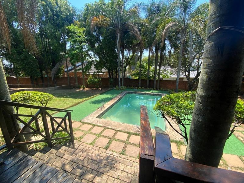 A private backyard featuring a swimming pool, paved patio area, and established garden with mature trees and brick boundary walls.