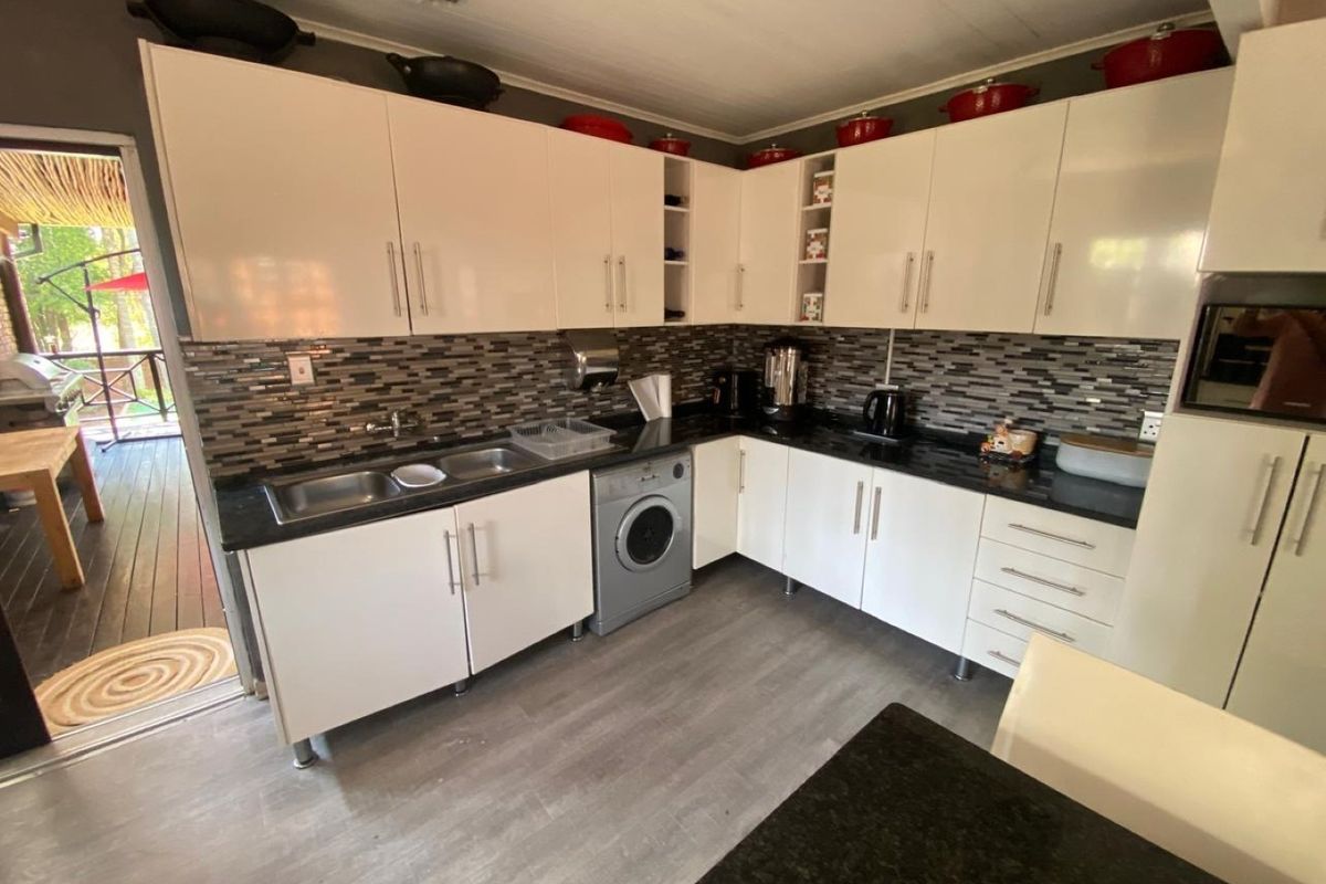 Modern kitchen featuring white cabinetry, dark laminate countertops, mosaic tile backsplash, and an integrated washing machine with direct access to an outdoor patio area.