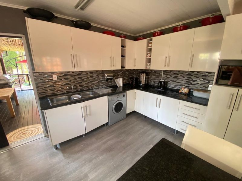 Modern kitchen featuring white cabinetry, dark laminate countertops, mosaic tile backsplash, and an integrated washing machine with direct access to an outdoor patio area.