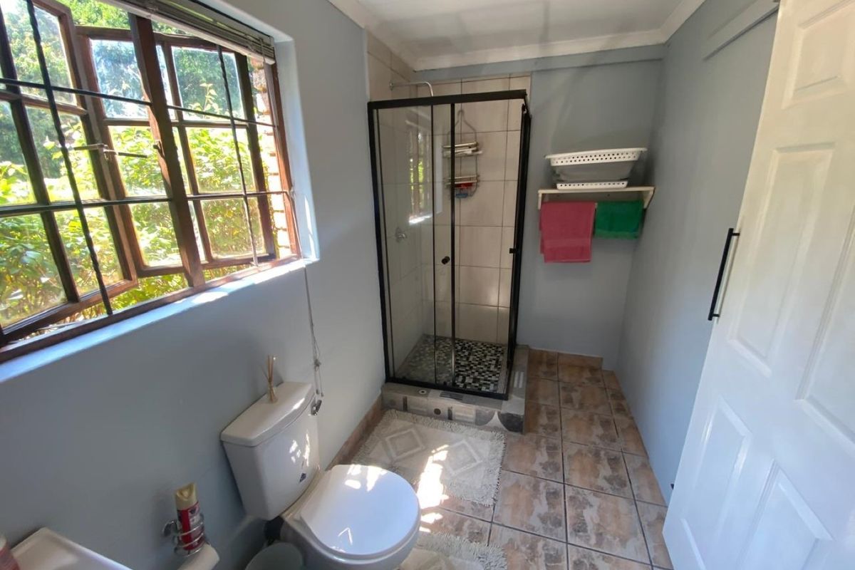 A functional bathroom featuring a shower enclosure, toilet, and tiled flooring, with natural light provided by a side-facing casement window.