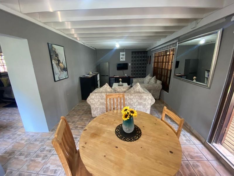 Open plan living and dining area featuring exposed beam ceilings, ceramic floor tiling, and a large wall-mounted mirror.