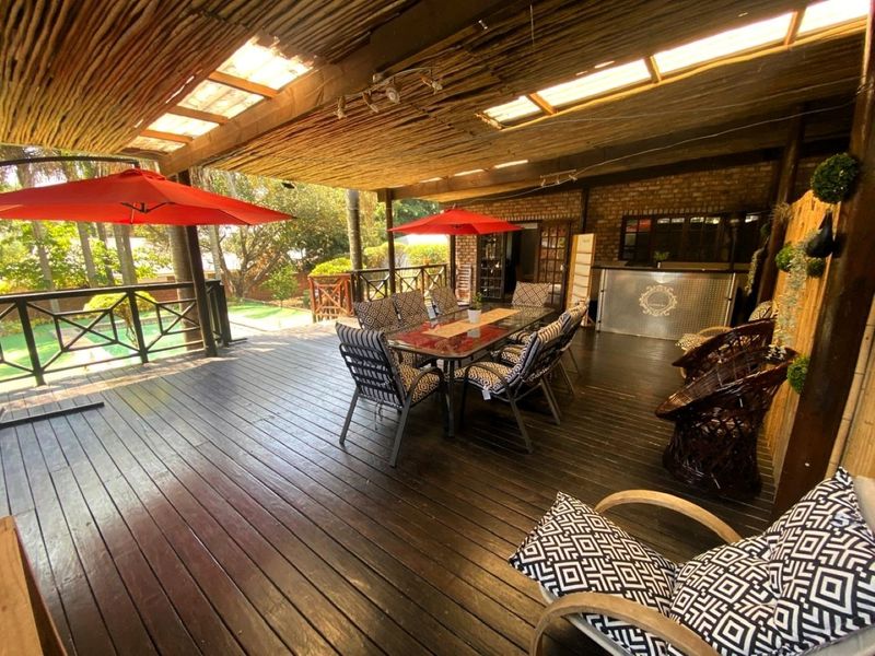 Spacious covered outdoor patio featuring timber decking, a rustic thatched roof, exposed brickwork, and a built-in bar area, ideal for entertaining.