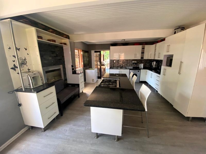 Spacious open-plan kitchen featuring a central island with gas hob, modern cabinetry, stone countertops, and an integrated fireplace area.