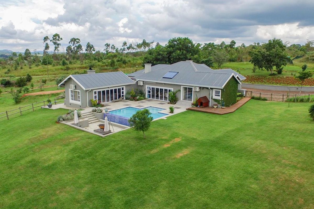 Aerial view of a well-maintained residence featuring a swimming pool, expansive lawn, timber decking, and modern bi-fold doors opening to the garden.