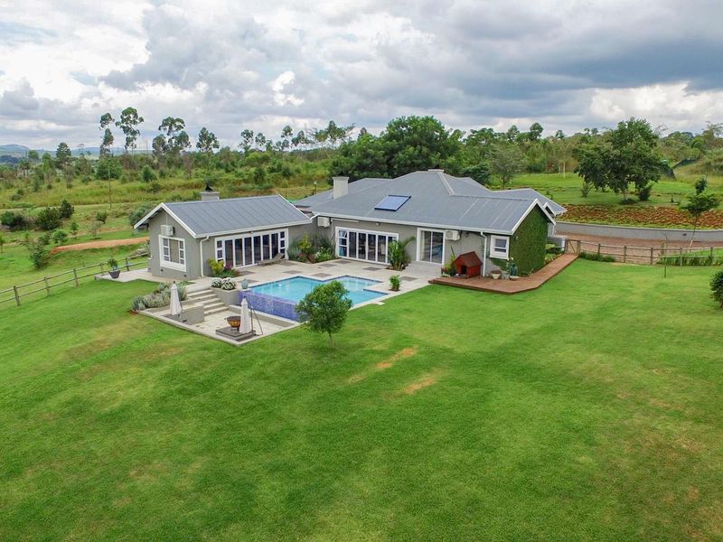 Aerial view of a well-maintained residence featuring a swimming pool, expansive lawn, timber decking, and modern bi-fold doors opening to the garden.