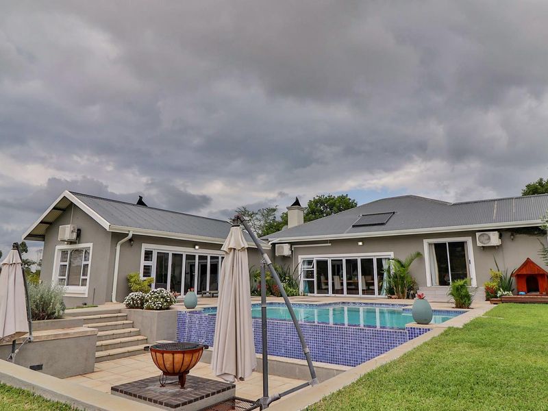 Rear exterior view featuring a swimming pool with tiled surround, bi-fold doors leading to the house, and solar heating panels on the metal roof.