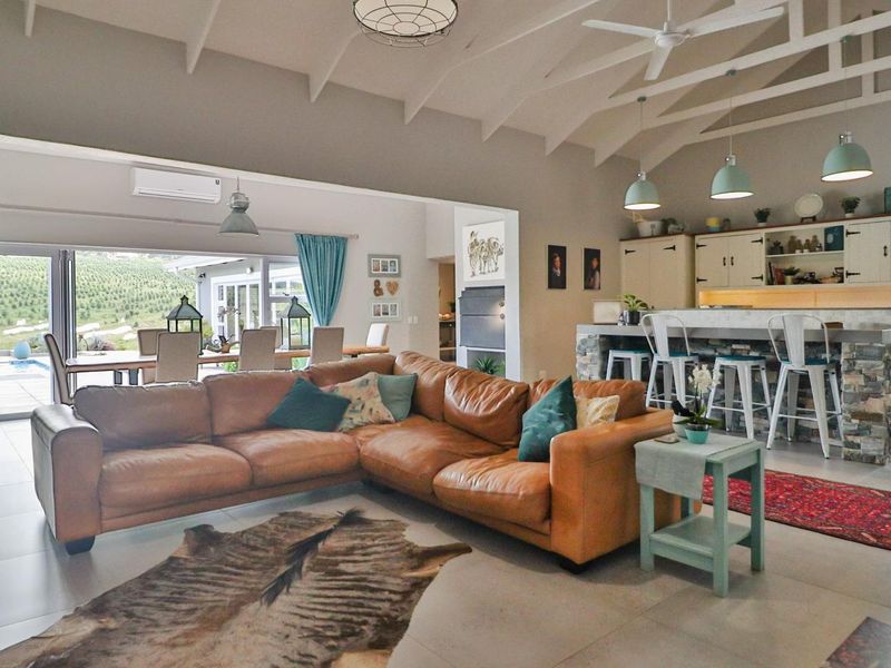 Spacious open-plan living and kitchen area featuring vaulted ceilings with exposed rafters, stone-clad island, and seamless flow to the outdoor patio through stacking doors.