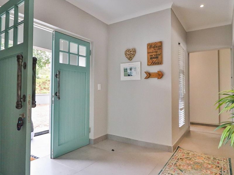 Bright and welcoming entrance hall featuring a distinctive light blue timber panelled front door, neutral tiled flooring, and recessed downlighting.