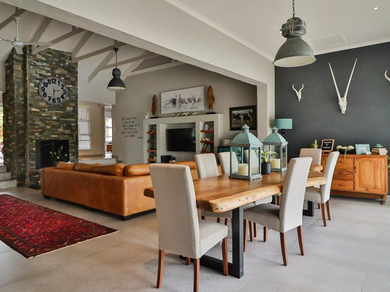 Spacious open-plan living and dining area featuring a striking stone-clad fireplace, vaulted ceilings with exposed rafters, and modern tiled flooring throughout.