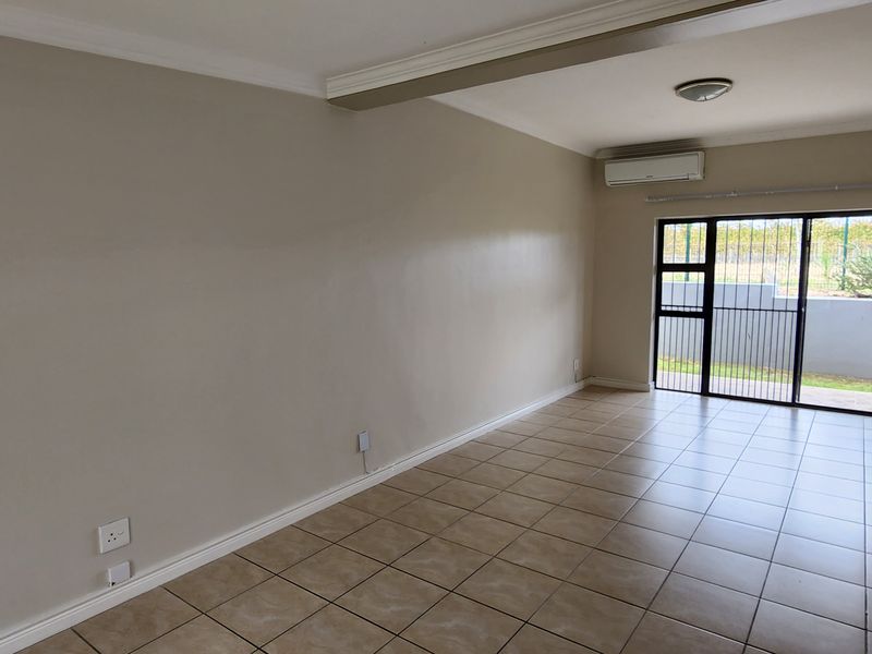 A spacious, empty living area featuring ceramic tile flooring, crown molding, a split-system air conditioner, and a sliding glass door leading to the exterior.