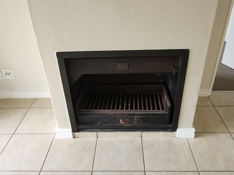 A vacant living area featuring a built-in fireplace with a metal grate and neutral ceramic floor tiling throughout.