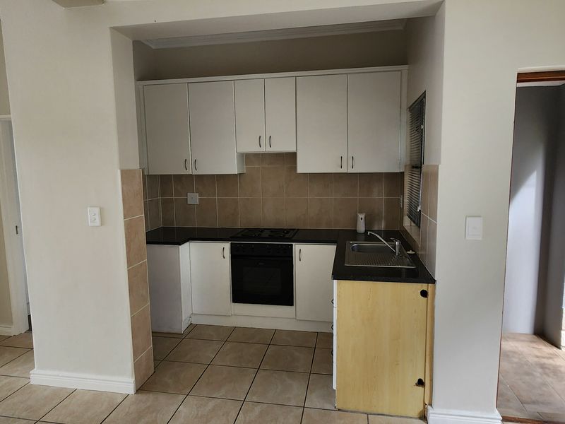 Compact kitchen featuring built-in cabinetry, black granite countertops, and integrated oven and hob, adjacent to a living area with a built-in fireplace.
