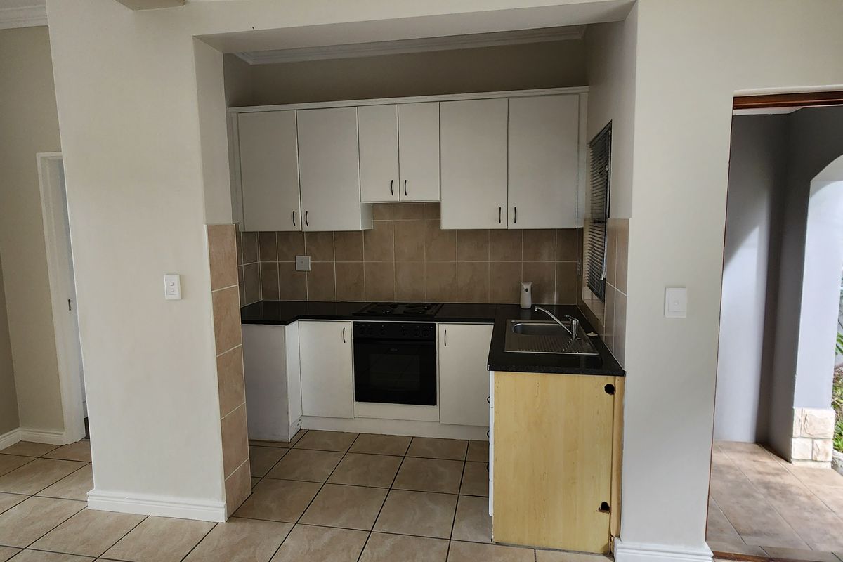 Compact kitchen featuring built-in cabinetry, black granite countertops, and integrated oven and hob, adjacent to a living area with a built-in fireplace.