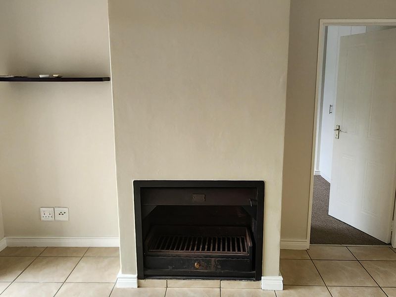 A bright living room featuring a central built-in fireplace, neutral ceramic floor tiles, and classic crown molding, offering a clean and versatile living space.