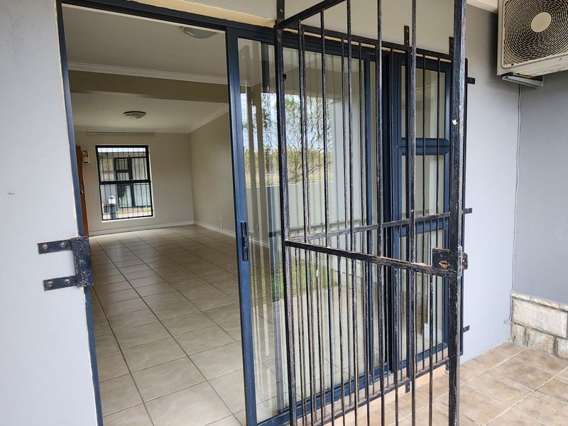 A covered patio area featuring tiled flooring, stone cladding, and a security gate, providing access to the interior living space.