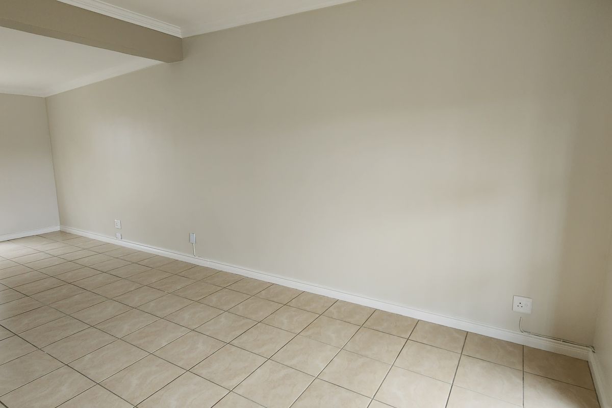 A bright, empty living room featuring neutral wall paint, ceramic floor tiles, and windows fitted with security bars.