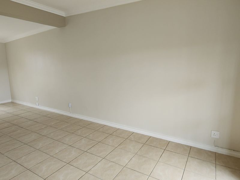 A bright, empty living room featuring neutral wall paint, ceramic floor tiles, and windows fitted with security bars.