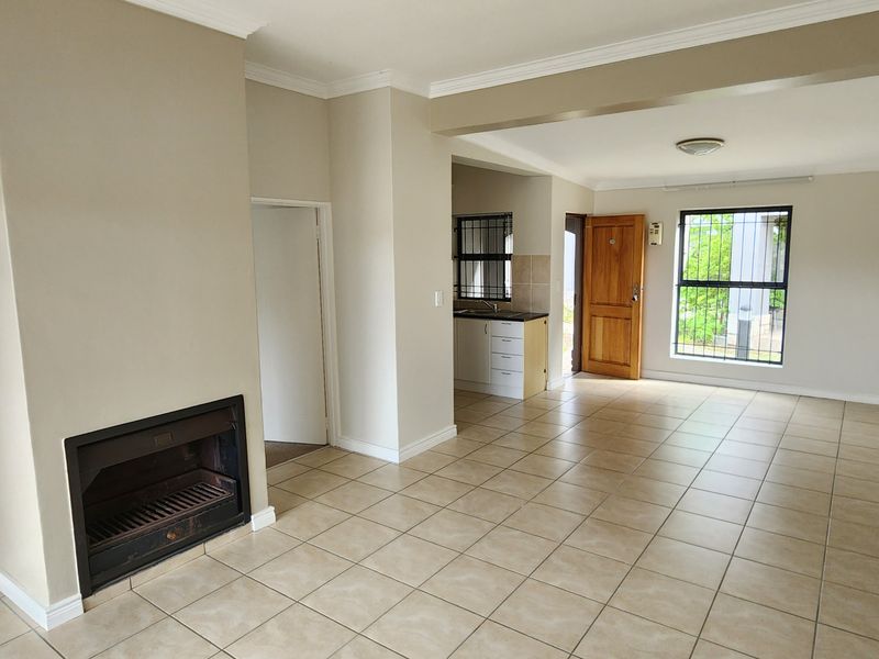 Spacious open-plan living area featuring a built-in fireplace, neutral ceramic floor tiles, and an adjoining kitchen space with functional cabinetry.