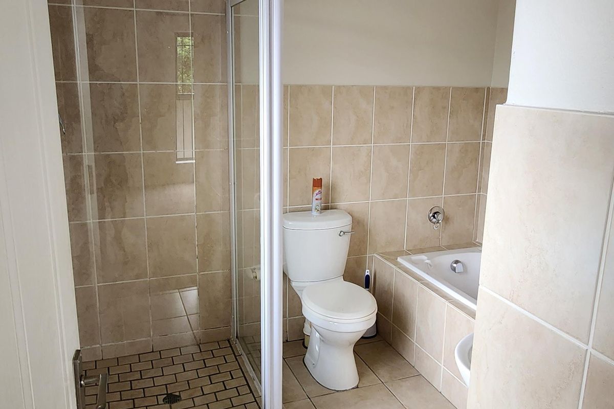 A functional bathroom featuring a separate shower enclosure, bathtub, toilet, and neutral ceramic wall and floor tiling.