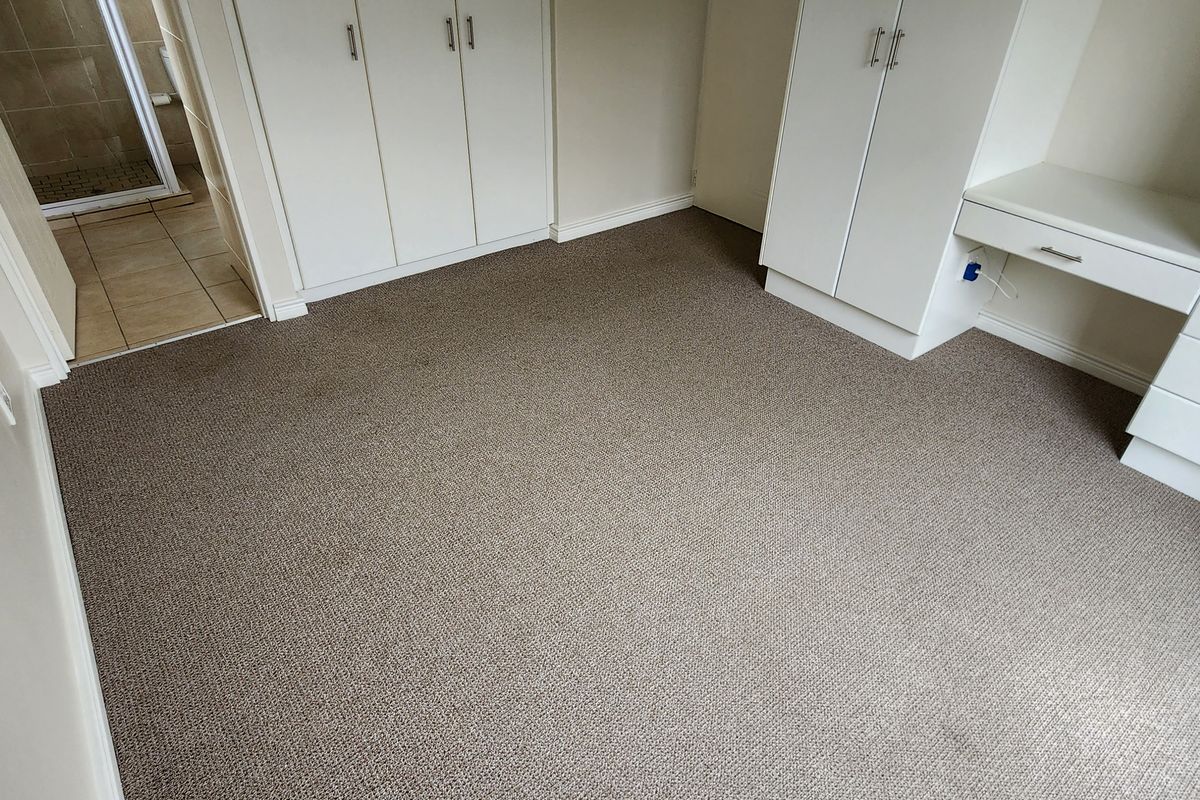 A clean, empty bedroom featuring neutral carpeting and extensive built-in cabinetry with an integrated desk area, offering ample storage and workspace.