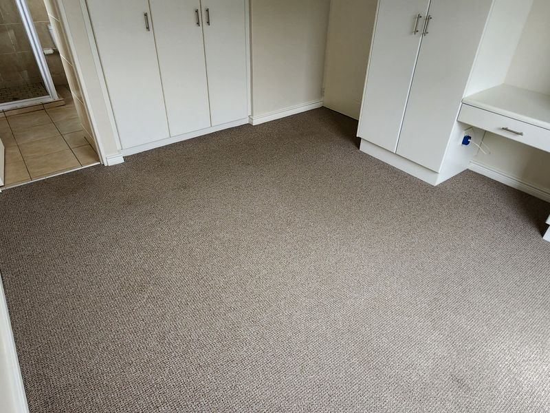 A clean, empty bedroom featuring neutral carpeting and extensive built-in cabinetry with an integrated desk area, offering ample storage and workspace.