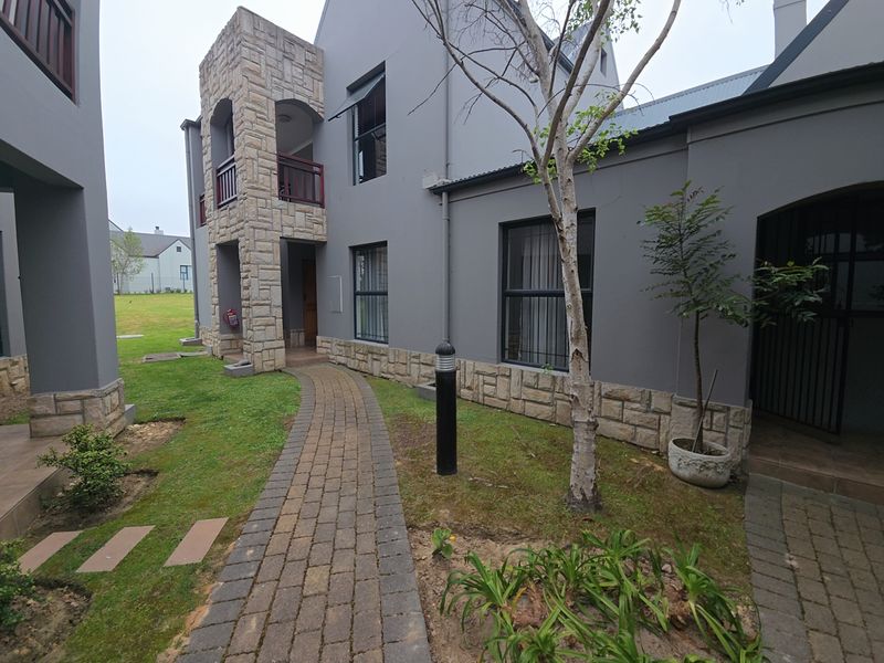 Exterior view of the apartment building featuring stone cladding, a paved walkway, and a small balcony area.