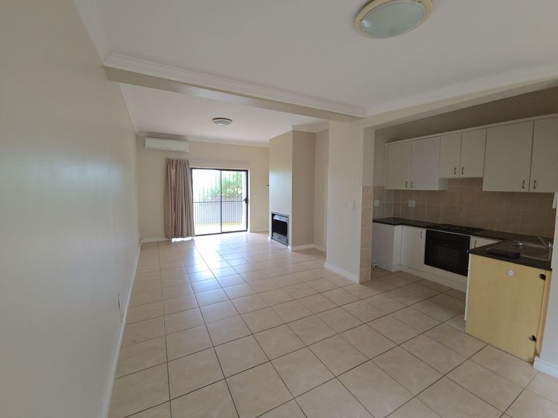 Open-plan living and kitchen area featuring tiled floors, a built-in fireplace, air conditioning, and a functional kitchen with built-in appliances.