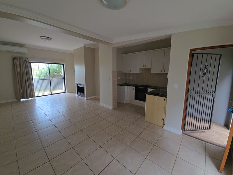 Spacious open-plan living and kitchen area featuring tiled floors, a built-in fireplace, and direct access to an outdoor space through sliding glass doors.