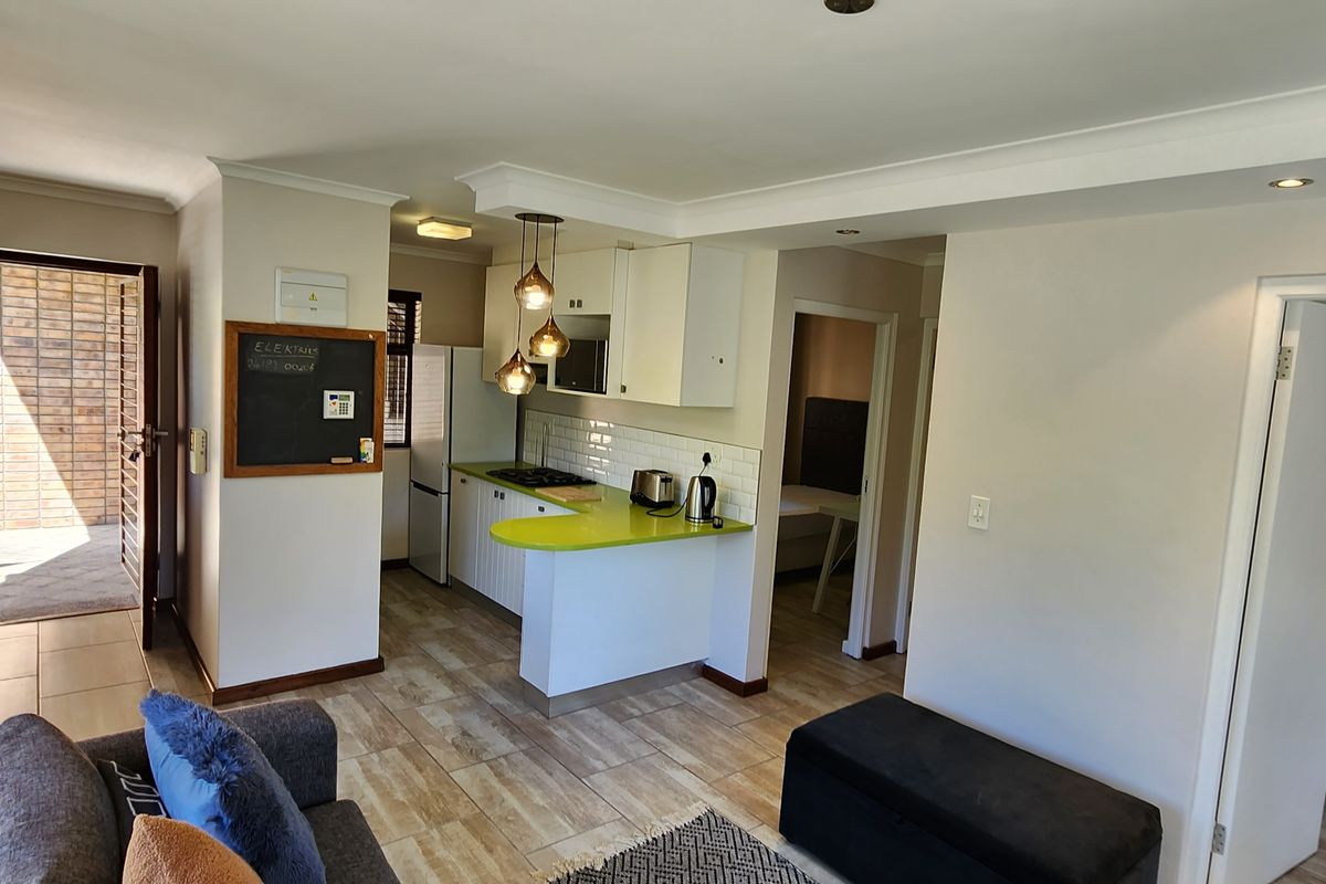 Open-plan living area featuring a compact kitchen with built-in cabinetry, a hob, and tiled flooring, leading to an outdoor patio area.