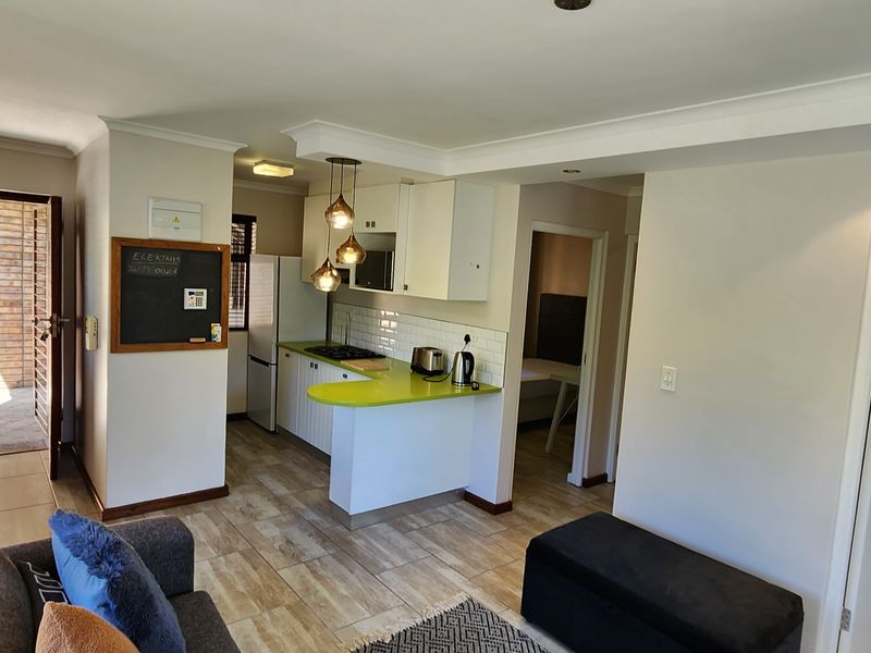 Open-plan living area featuring a compact kitchen with built-in cabinetry, a hob, and tiled flooring, leading to an outdoor patio area.