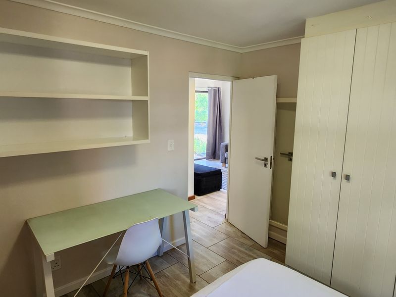 A bedroom featuring built-in cupboards, wall-mounted shelving, and tiled flooring, with a doorway leading to an adjacent living space.