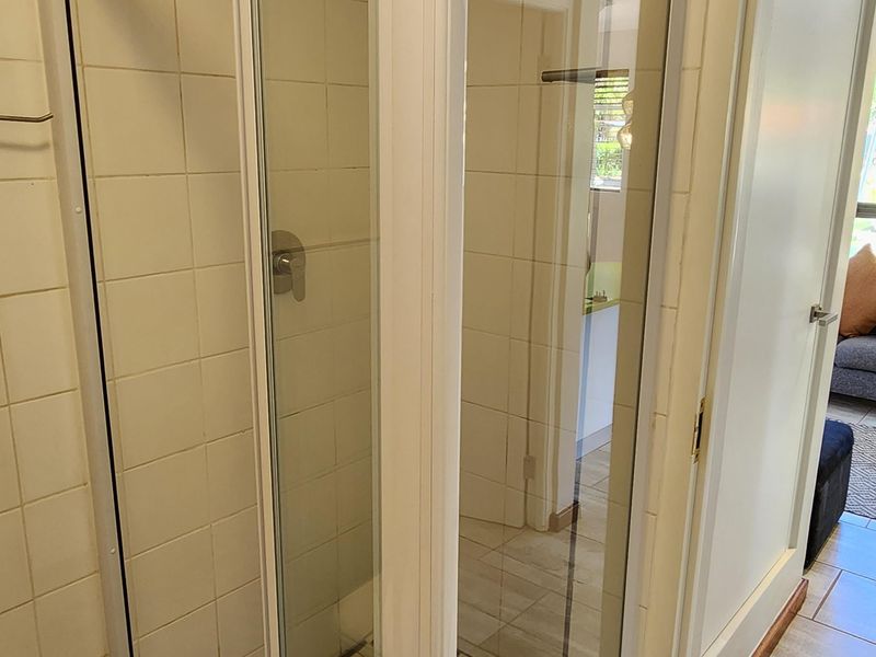 A functional bathroom featuring a corner shower enclosure with tiled walls and flooring, providing a clean and practical space.