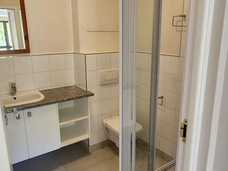 A functional bathroom featuring a vanity with granite countertop, wall-mounted toilet, and a glass-enclosed shower with tiled finishes.