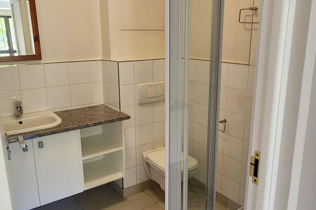 A functional bathroom featuring a vanity with granite countertop, wall-mounted toilet, and a glass-enclosed shower with tiled finishes.