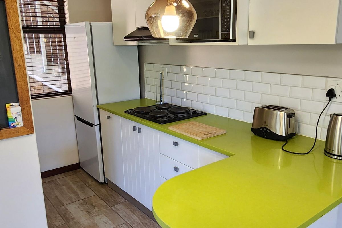 A compact kitchen featuring white cabinetry, a vibrant lime green countertop, subway tile backsplash, and modern pendant lighting over a breakfast bar area.