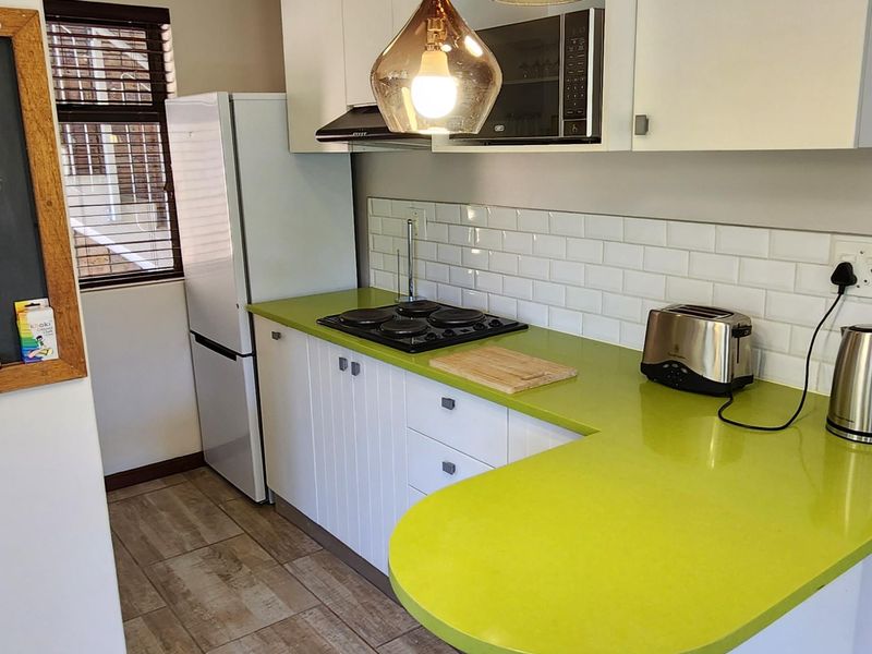 A compact kitchen featuring white cabinetry, a vibrant lime green countertop, subway tile backsplash, and modern pendant lighting over a breakfast bar area.