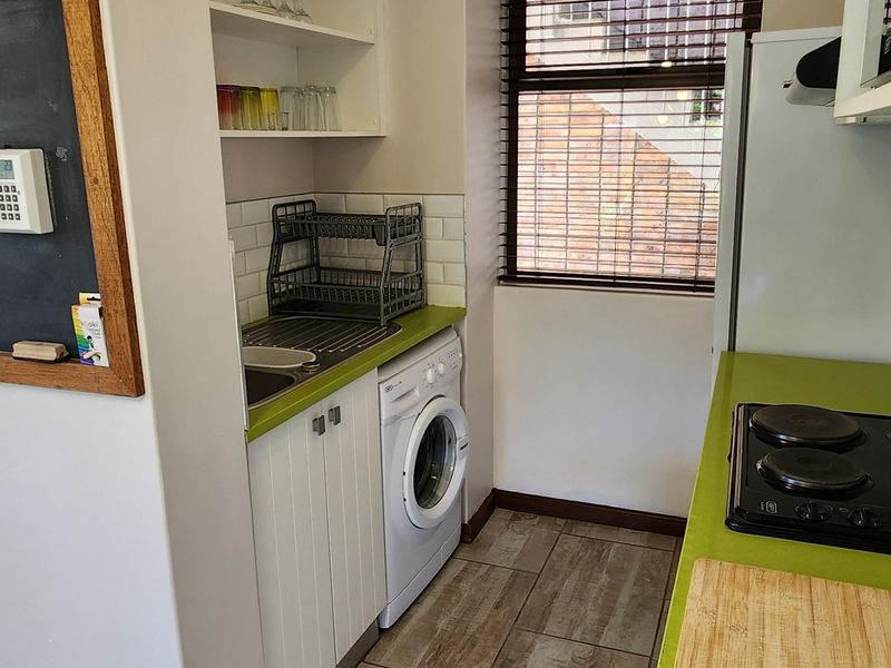 Compact kitchen featuring built-in cabinetry, a hob, tiled flooring, and integrated laundry space with a sink and shelving.