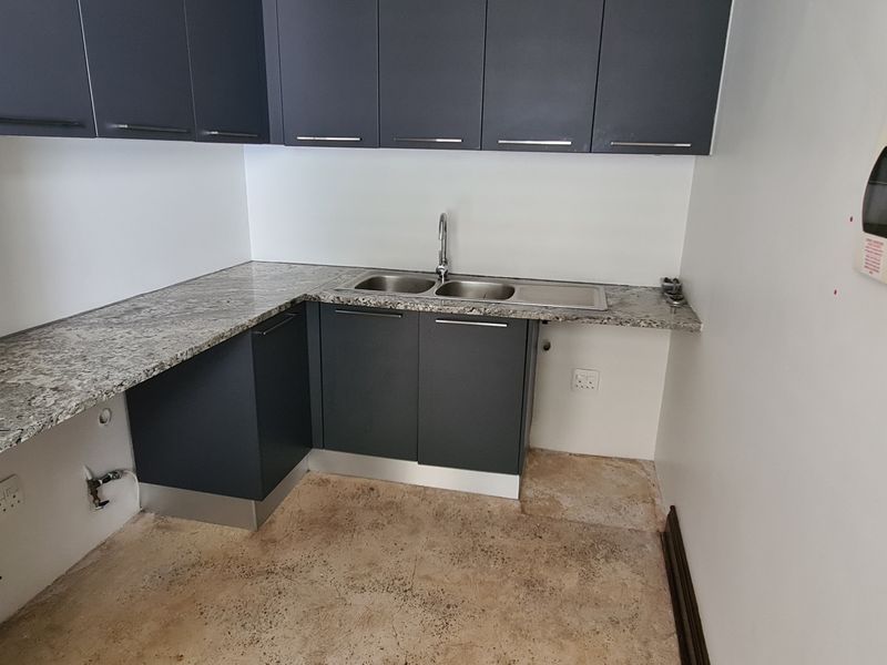 A functional scullery area featuring dark grey cabinetry, granite countertops, a double stainless steel sink, and visible plumbing connections for appliances.