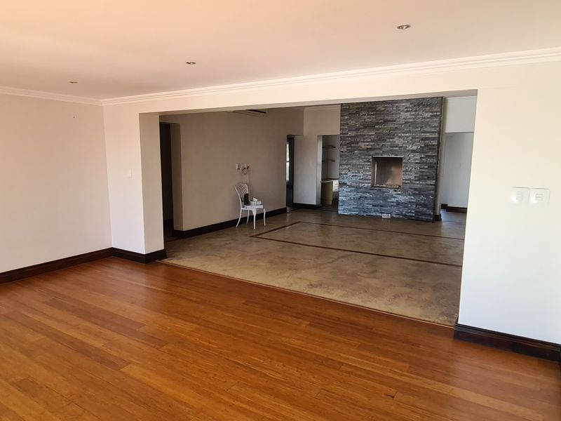 Spacious open-plan living area featuring a combination of hardwood and polished concrete flooring, complemented by a striking stone-clad fireplace and recessed lighting.